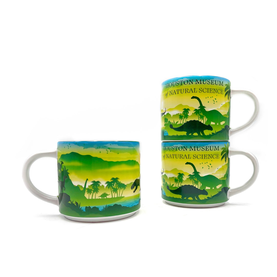 Two mugs with dinosaur and nature design, stacked on a white background with another mug showing the reverse side in the foreground.