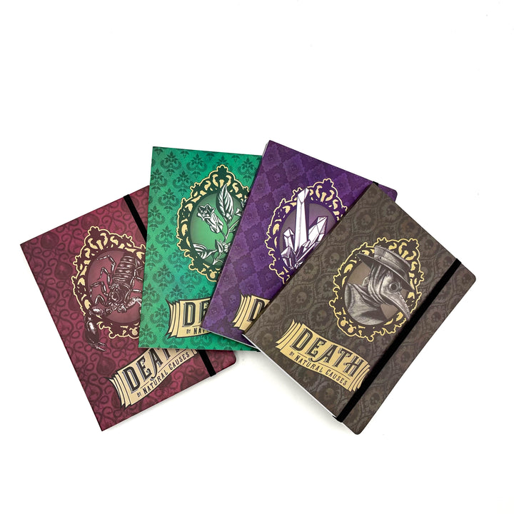 four softbound journals in red, green, purple, and black are spread across a white background