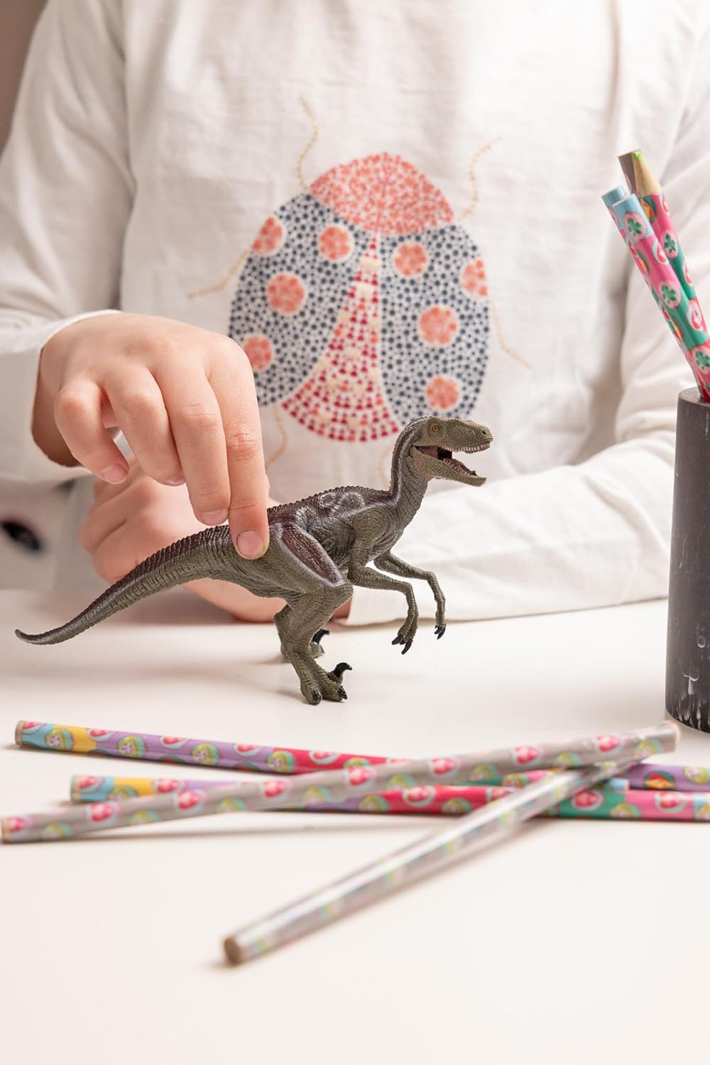 Velociraptor Dinosaur Replica Toy being played with child, with colorful pencils surrounding the toy
