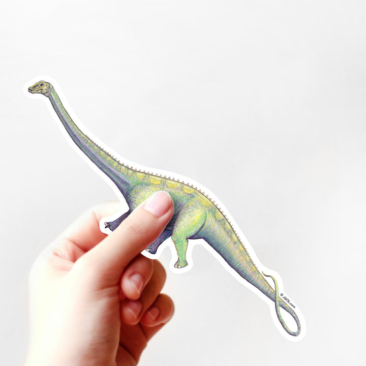 Hand holding a colorful dinosaur sticker against a white background