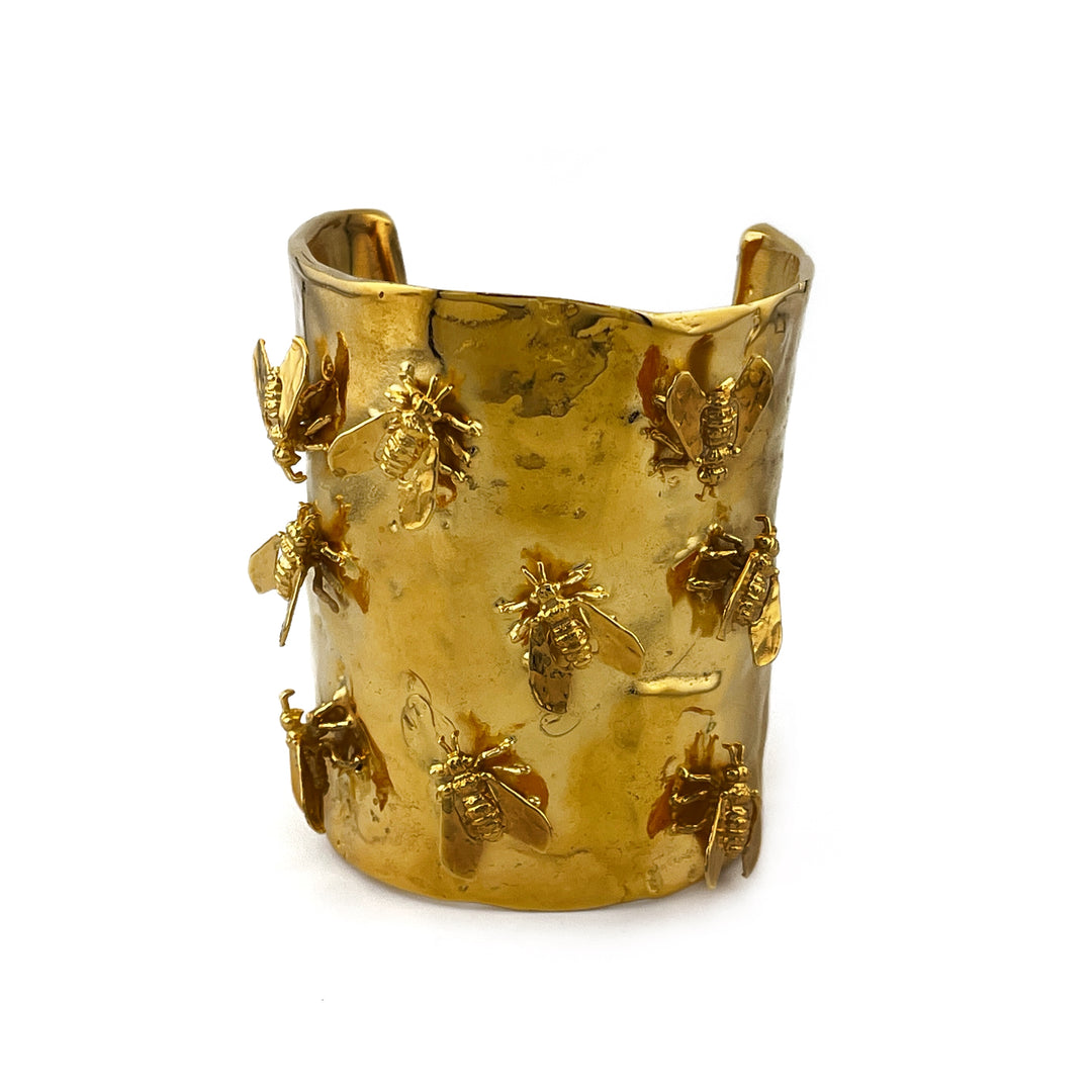 Gold cuff bracelet with bee designs on a white background