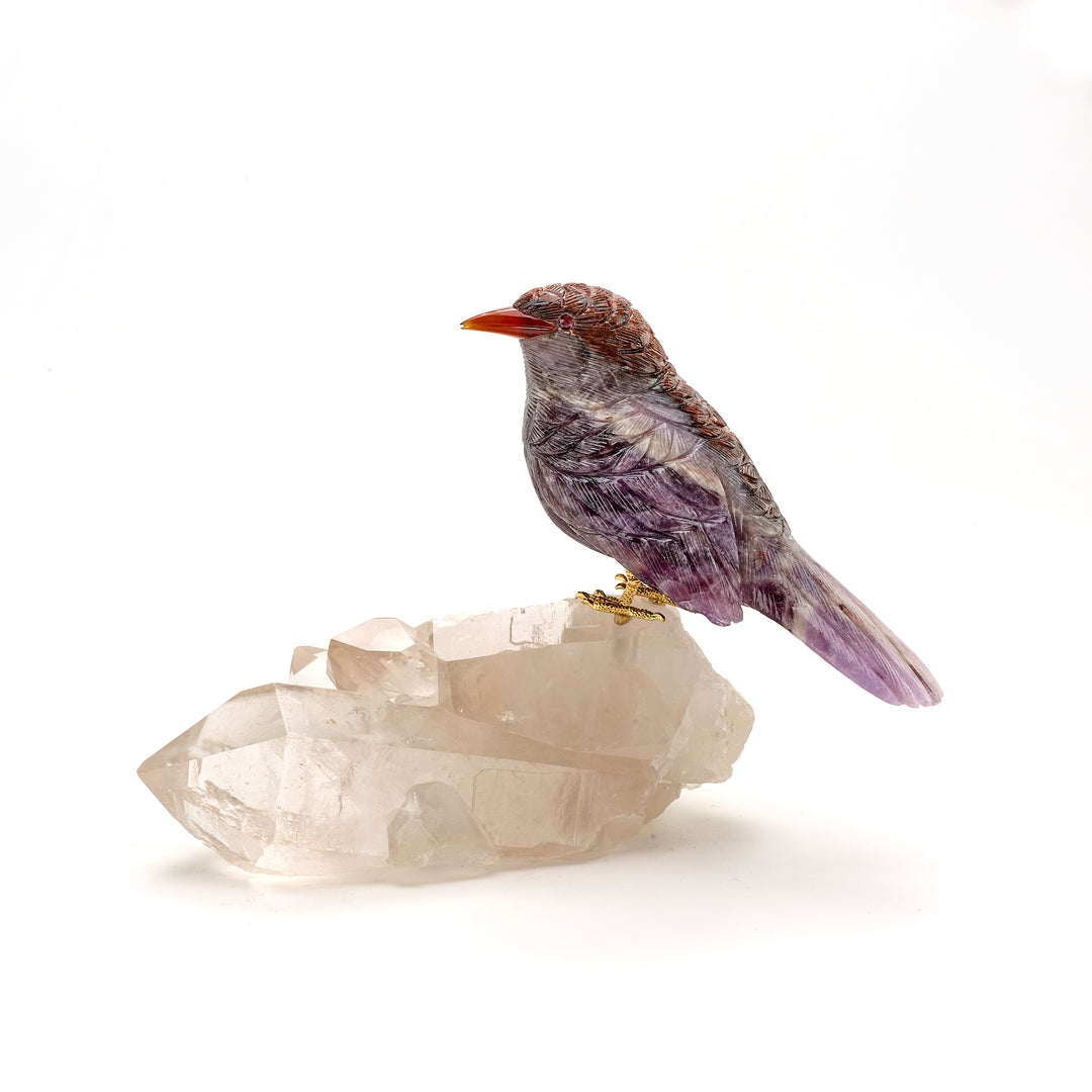 A carved amethyst and feldspar wren bird with garnet eyes and an agate beak perched on a clear quartz crystal.