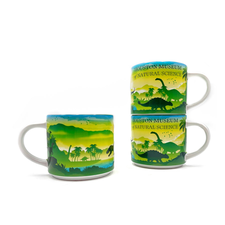 Two mugs with dinosaur and nature design, stacked on a white background with another mug showing the reverse side in the foreground. 