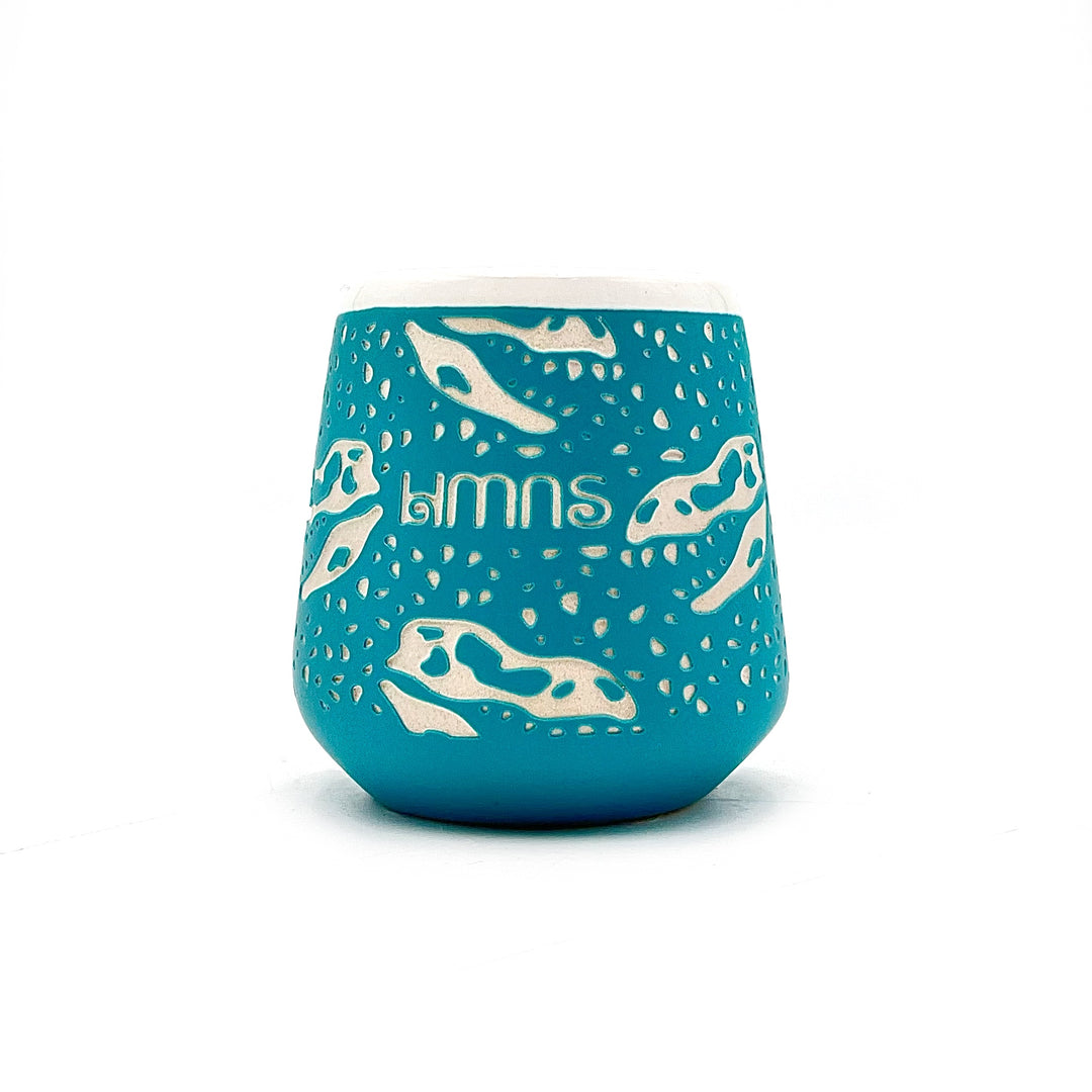 Blue ceramic shot glass with white dinosaur illustrations on a white background