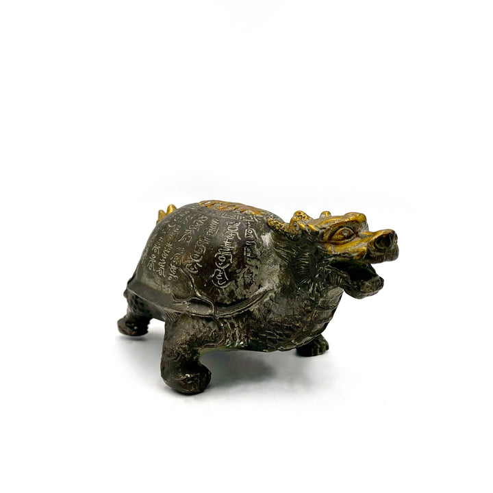 Small bronze figurine of a dragon with the shell of a turtle, covered in gold and patina green accents on a white background