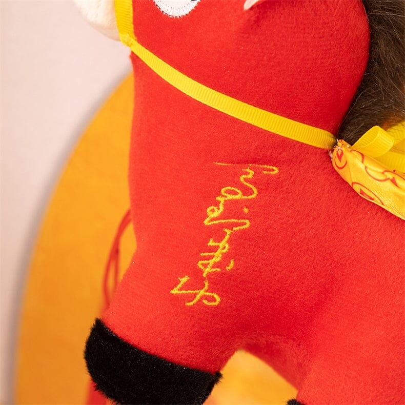 Red plush toy with yellow accents and embroidered text on a beige background