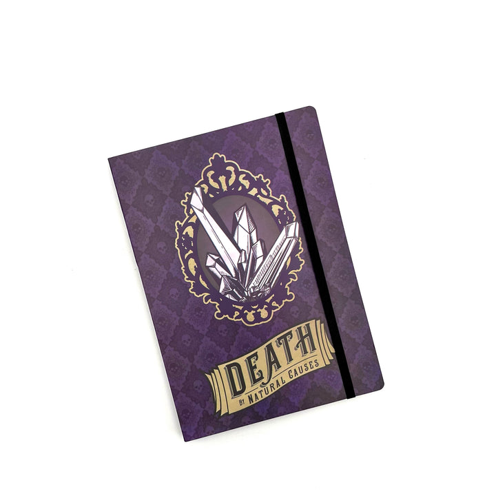 a purple softbound notebook with a graphic of a crystal and the exhibit name "death by natural causes" on the front cover, photographed against a white background