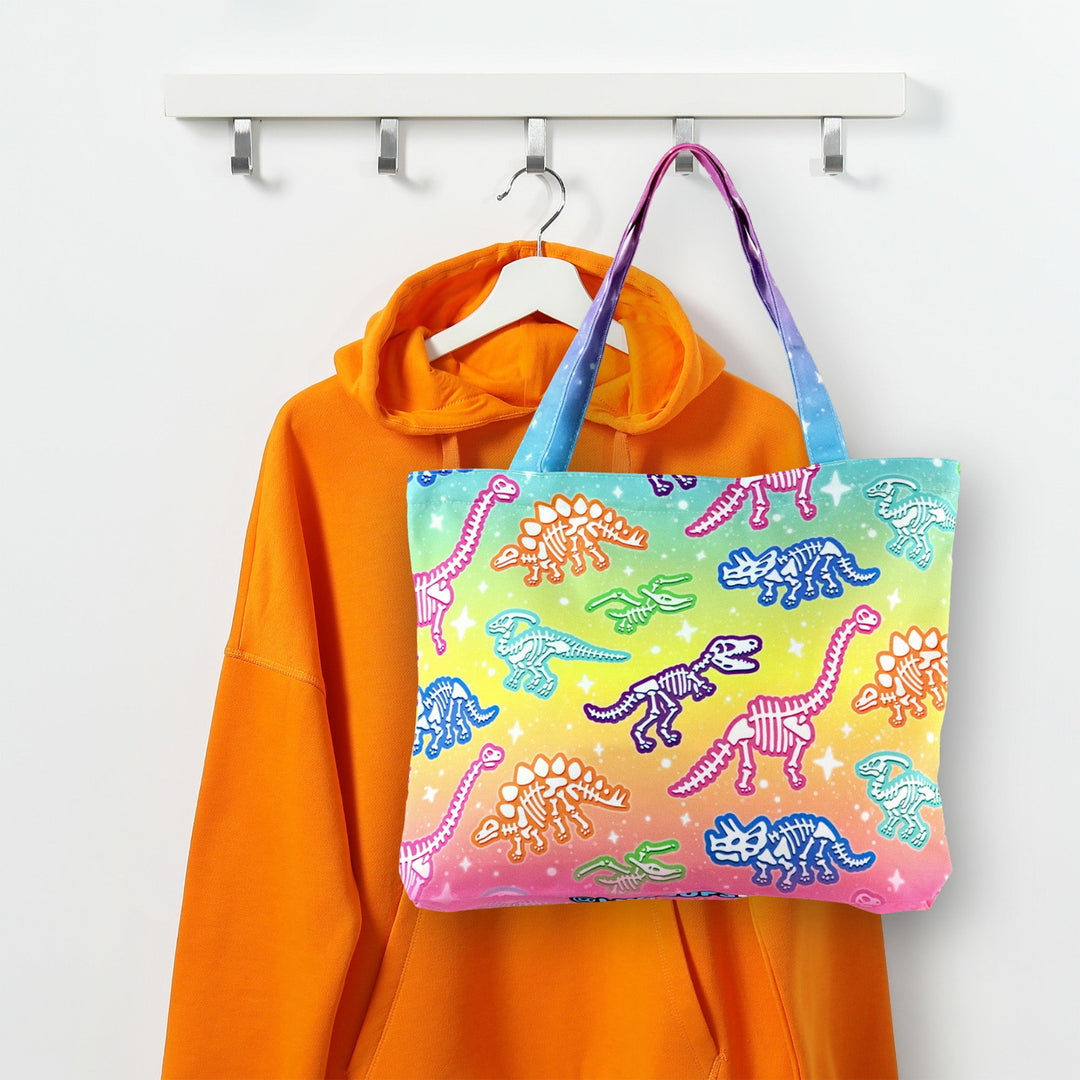 Colorful dinosaur-patterned tote bag hanging on a hanger with an orange hoodie.
