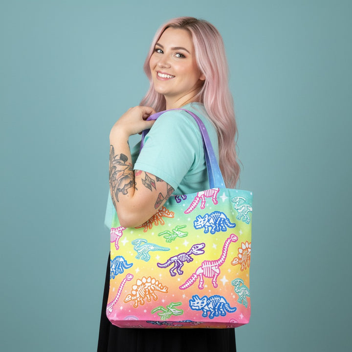 Woman holding a colorful tote bag with dinosaur design against a solid background