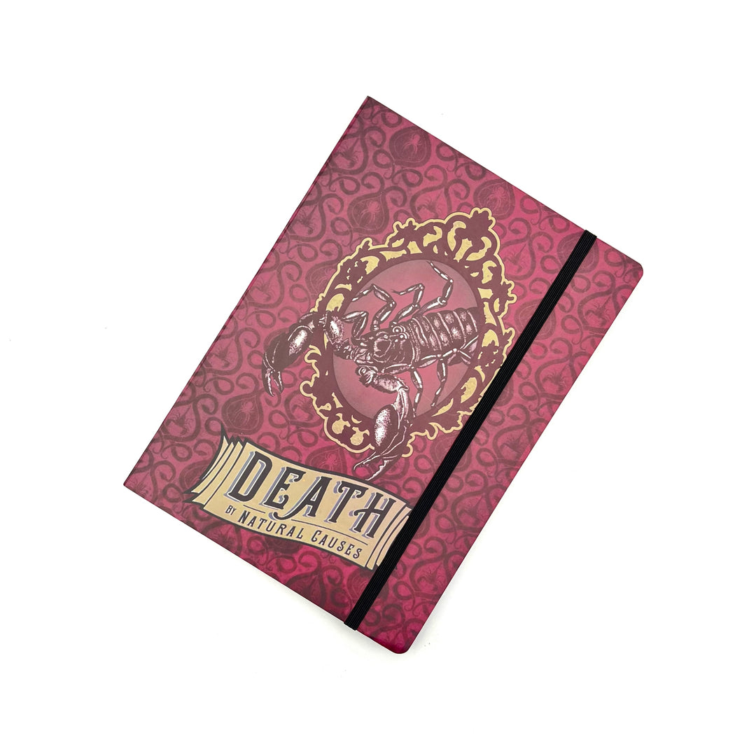 a red softbound journal featuring a scorpion graphic and the name of the exhibit "Death by natural causes" on the cover, photographed against a white background
