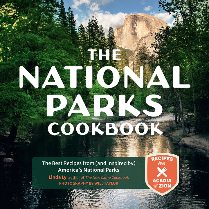Cover of 'The National Parks Cookbook' featuring a scenic view of a national park with green trees and a body of water in the foreground, and the title text superimposed on top.