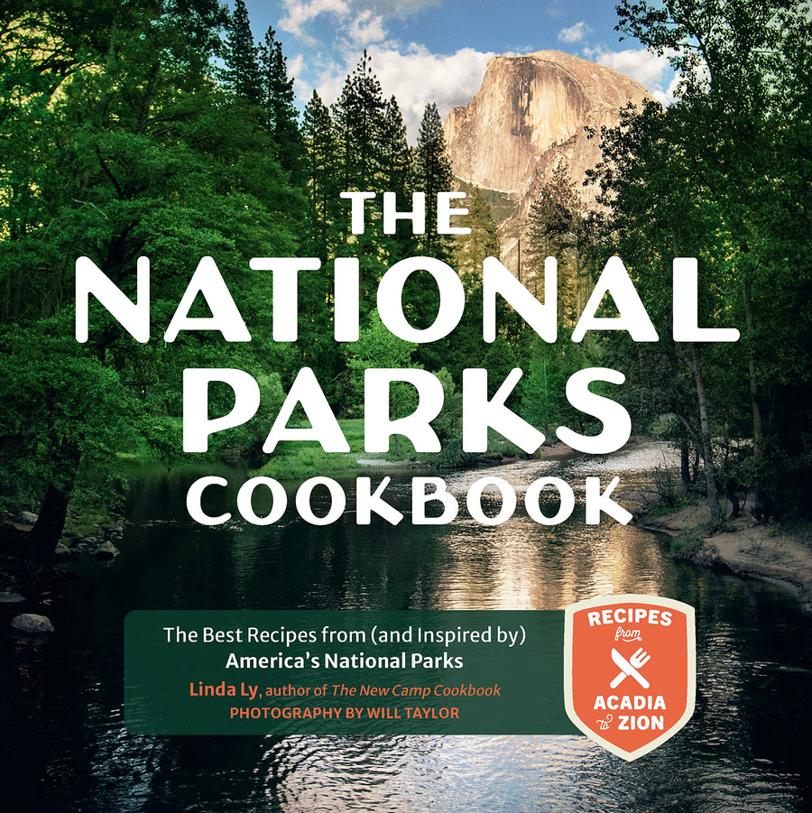 Cover of 'The National Parks Cookbook' featuring a scenic view of a national park with green trees and a body of water in the foreground, and the title text superimposed on top.
